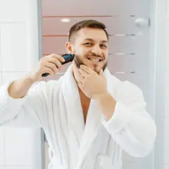 Mężczyzna w białym szlafroku goli zarost trymerem.