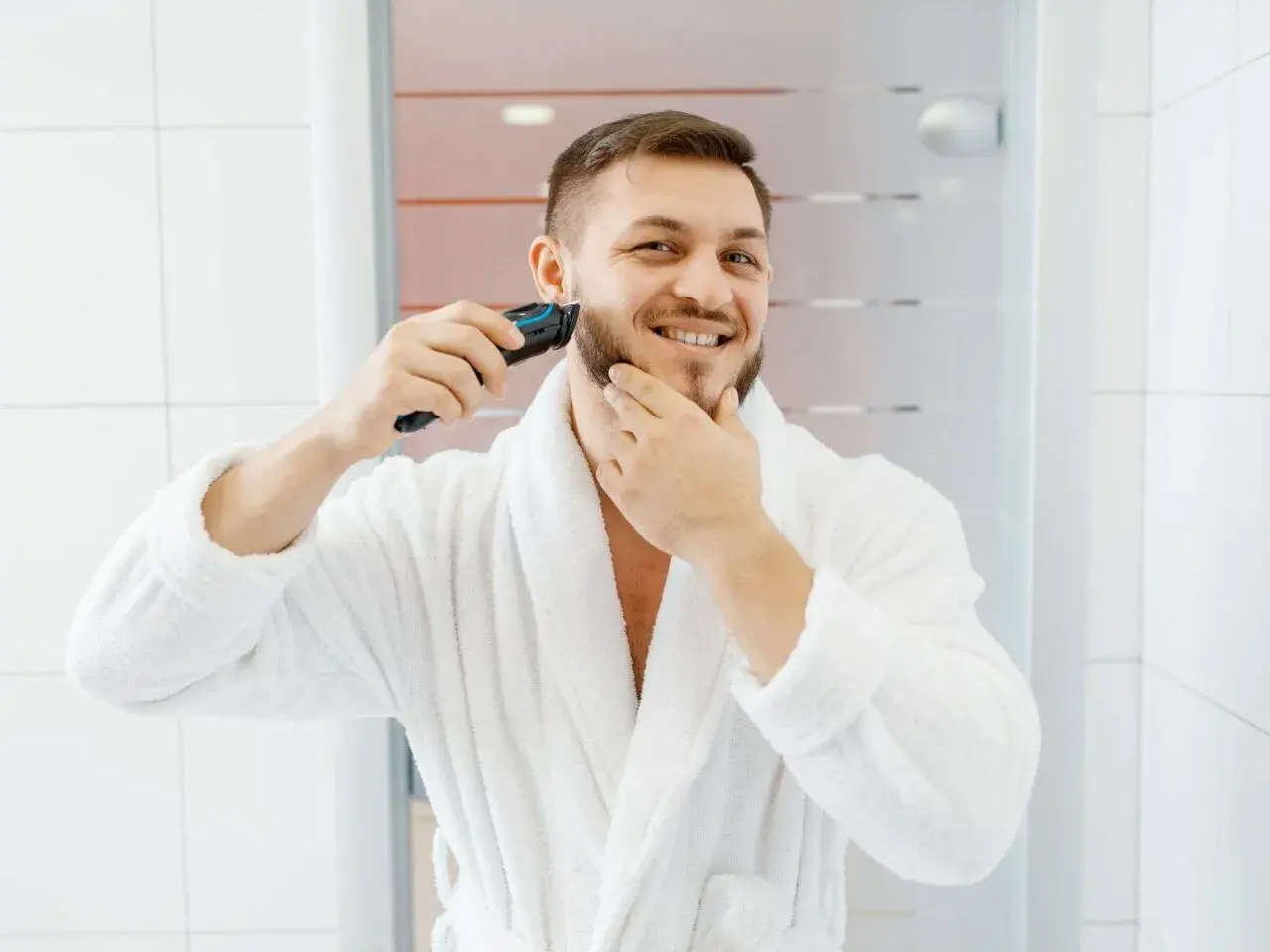 Mężczyzna w białym szlafroku goli zarost trymerem.